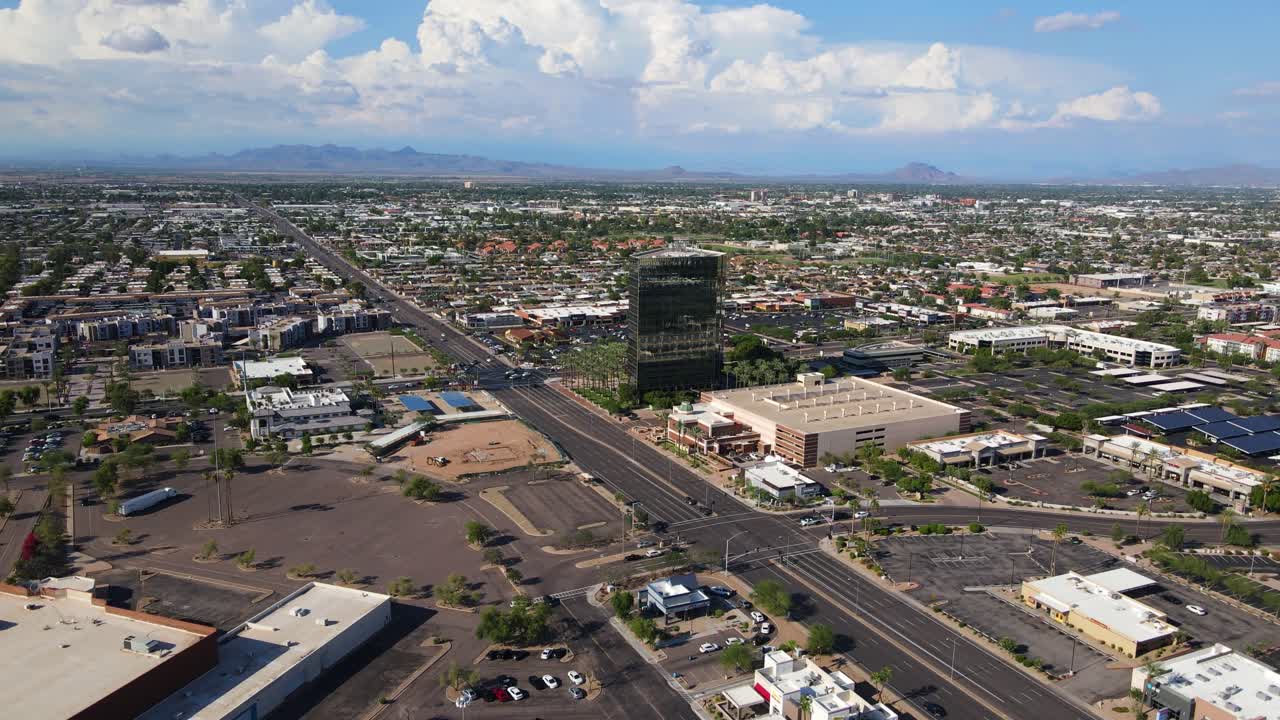 Drone 4K in volo verso un piccolo grattacielo a Mesa, Arizona, circondato da palme, montagne sullo sfondo e grandi nubi cumulonembi nel cielo