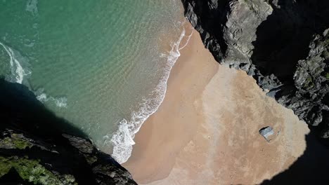 Cornish-Beach-Cove-Surrounded-by-Rocky-Cliffs-and-Turquoise-Waters-Rolling-Over-the-Sand-in-Cornwall,-UK