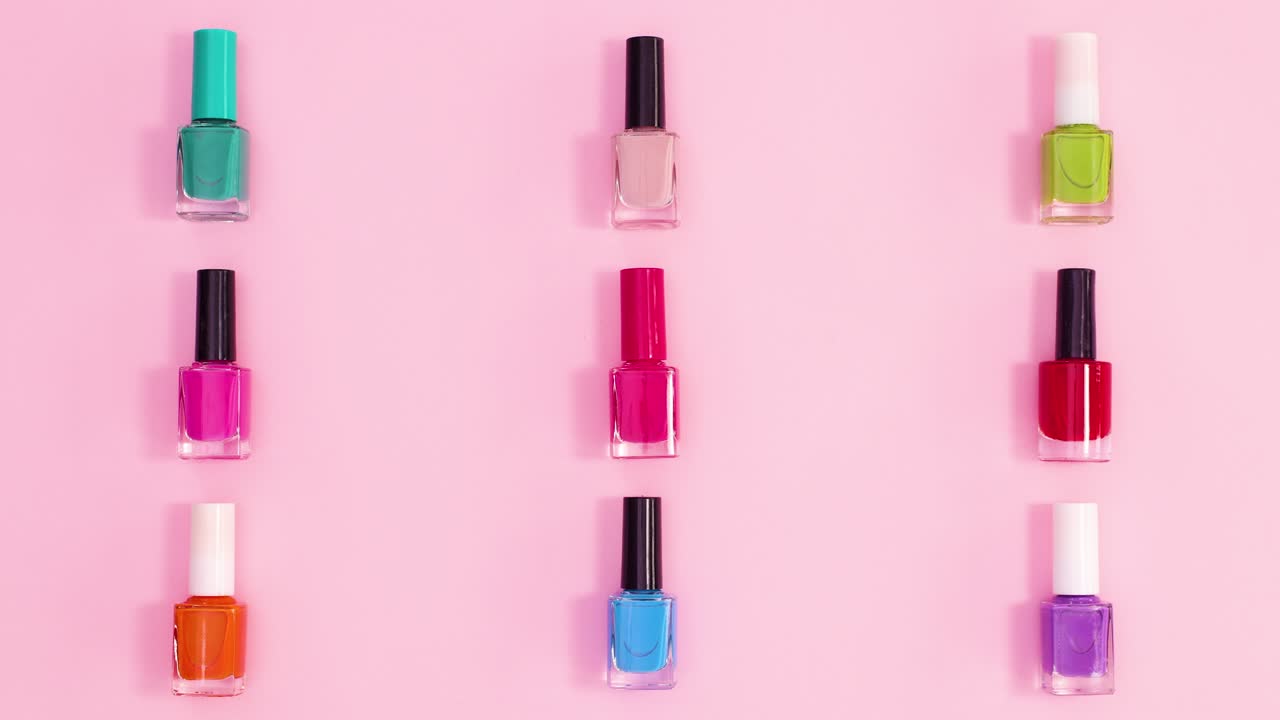 patrón creativo hecho de manicura botellas de esmalte de uñas en diferentes colores se mueven en fondo rosa pastel. detener el movimiento