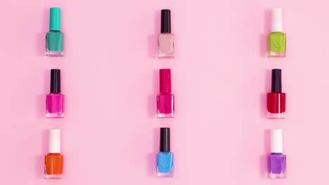 creative pattern made of manicure nail polish bottles in different colors move on pastel pink background. stop motion