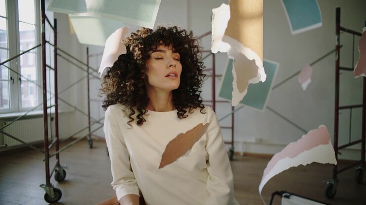 Modella che Reagisce con Top Chiaro, Inclinando e Chiudendo gli Occhi su una Sedia in Studio con Carta Strappata che Fluttua