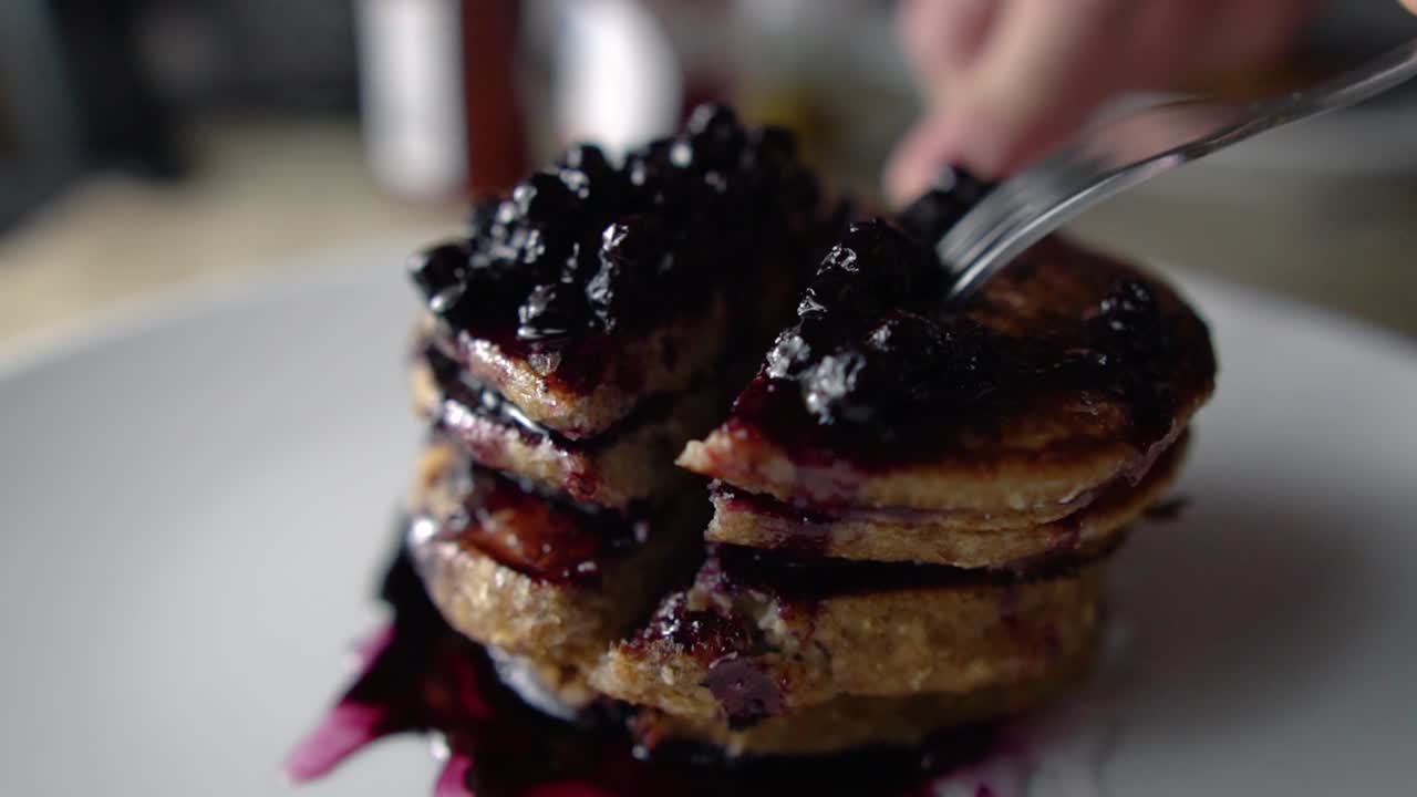 Cutting four stacked blueberry pancakes with metallic cutlery, SLOW MOTION