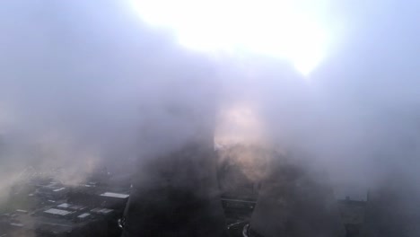 aerial view of partial uk power station cooling towers through dense smoke steam emissions at sunrise