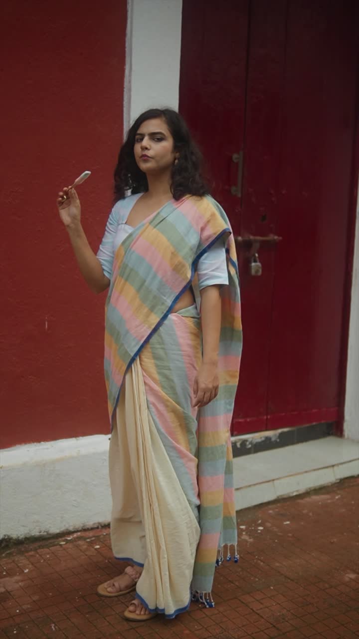 Side view of woman in pastel saree enjoying a lollipop, standing by red and white wall. India