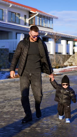 proud bearded caucasian father walks with his little baby boy. father and son wearing black and sunglasses outdoors. vertical video.