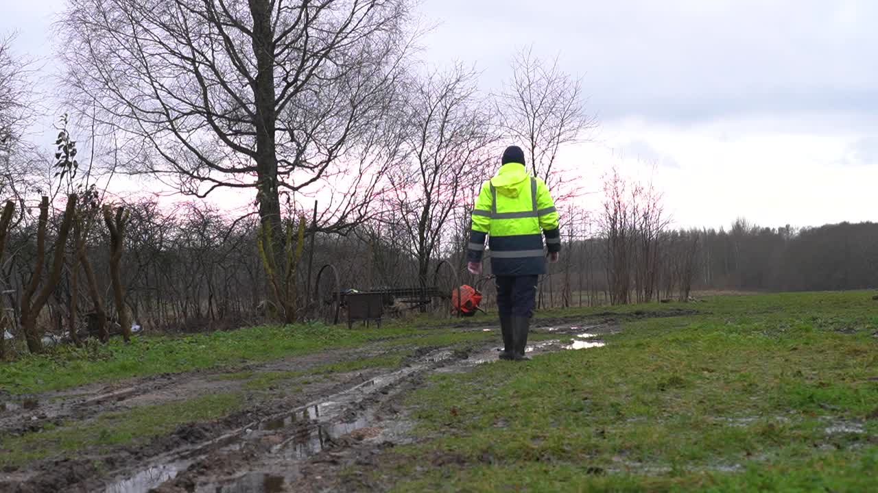 hombre en uniforme amarillo de seguridad se aleja cerca de la propiedad privada fangosa camino de tierra