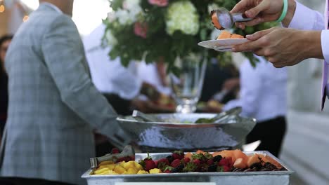 Invitado-Pone-Una-Rodaja-De-Fruta-Exótica-En-Un-Plato-Del-Elegante-Buffet-De-Recepción-Nupcial