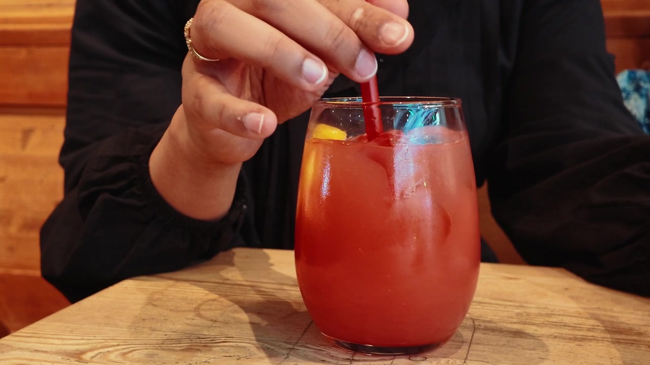 Persona che mescola un rinfrescante cocktail rosso con una cannuccia