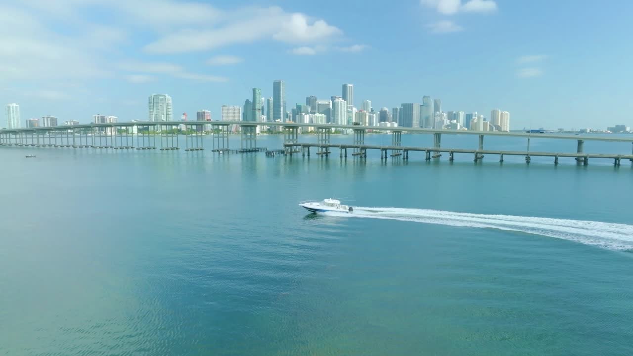 el yate está navegando a lo largo del puente a través del mar azul, con la ciudad de miami, florida, en el fondo