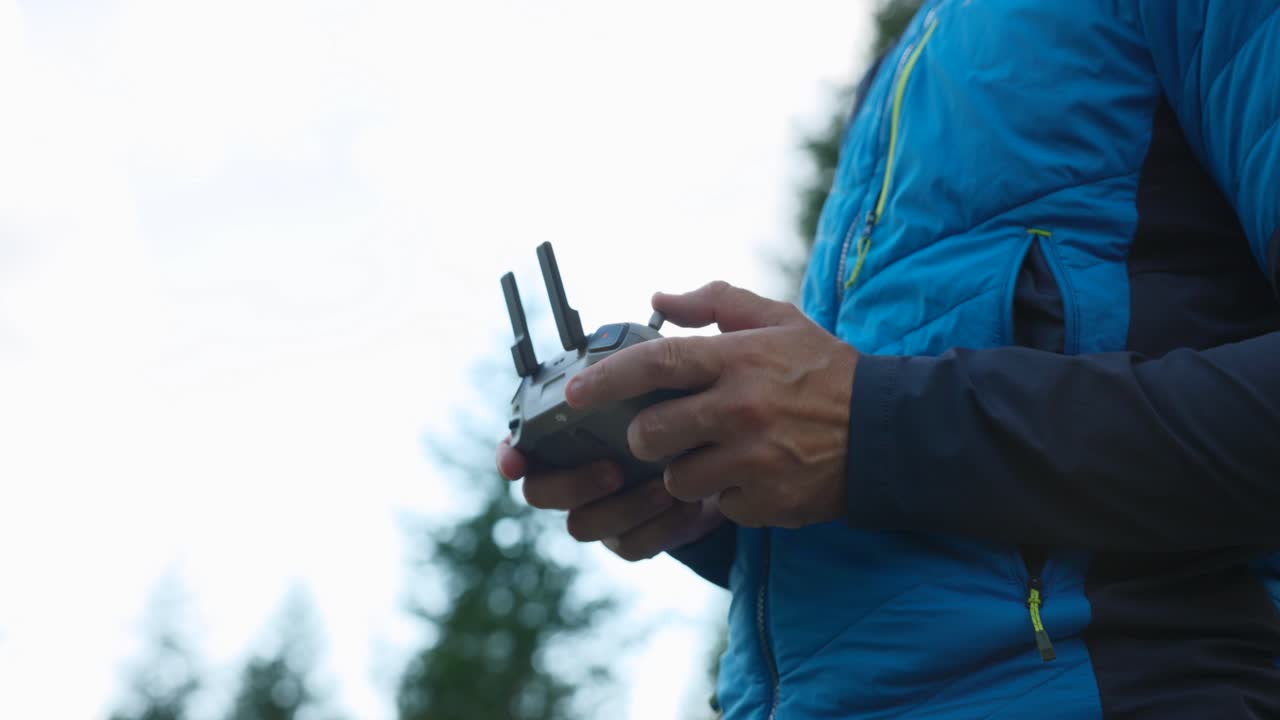 bajo ángulo de primer plano del piloto que sostiene el controlador mientras el quadcopter vuela por encima