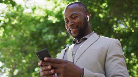 Happy-african-american-man-in-city-wearing-earphones-and-using-smartphone