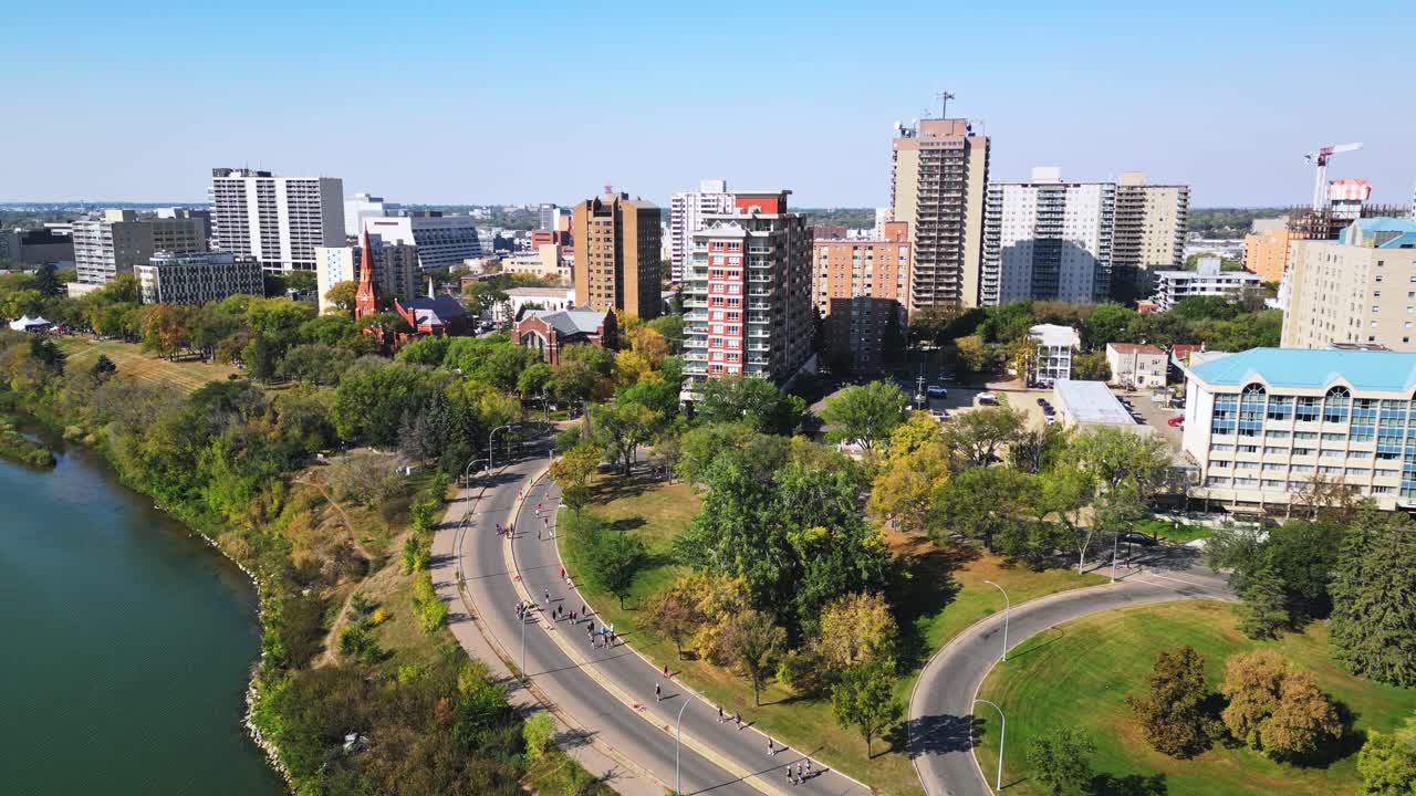 Drone view shows marathon runners by Saskatoon riverfront under clear blue sky
