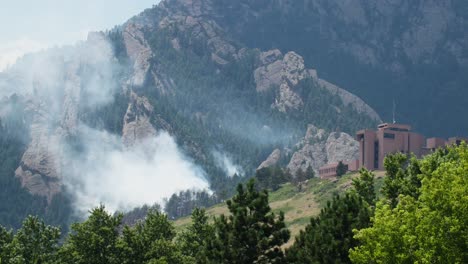 wildfire smoke rising from a forest near mountains and a building