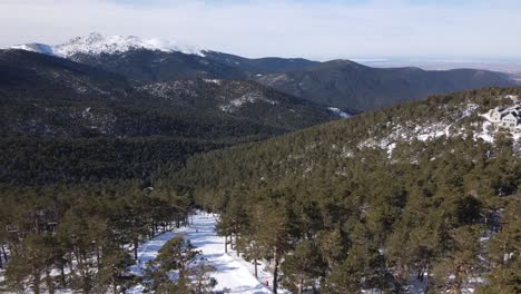 Espectacular-Vista-Aérea-De-La-Zona-De-Esquí-De-Navacerrada-En-Madrid,-España,-Con-La-Sierra-De-Guadarrama-Al-Fondo-Y-Gente-Esquiando-En-Primer-Plano