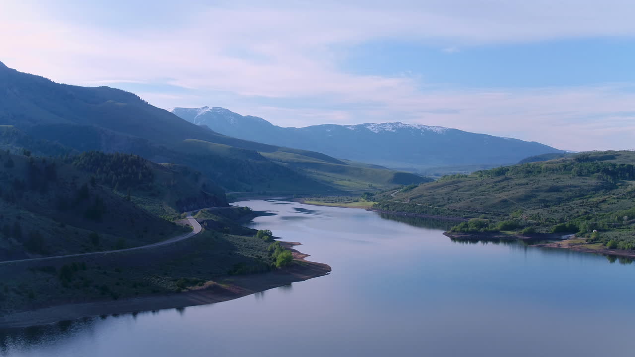 멀리 눈 덮인 산들과 콜로라도 호수 저수지 위로 날아가는 이른 아침 공중 드론