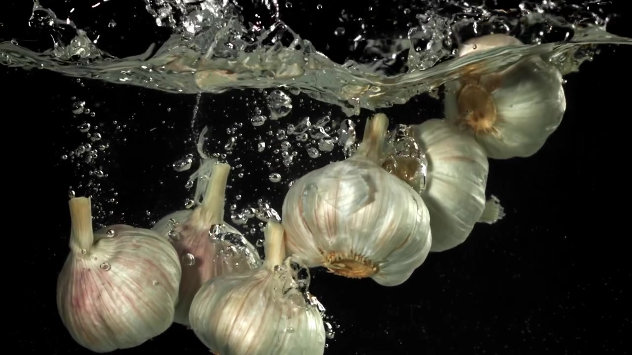 Bulbi d'aglio freschi che cadono nell'acqua al rallentatore