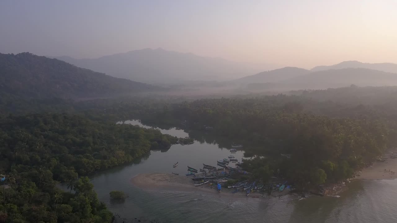 volando hacia un océano pacífico con barcos de madera atracando en un bosque espesor durante una mañana brumosa en la playa de palolem en canacona, goa del sur, india