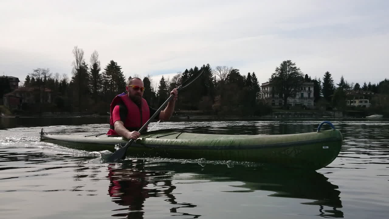 POV footage of adult man with yellow sunglass and red life jacket rowing kayak in a lake