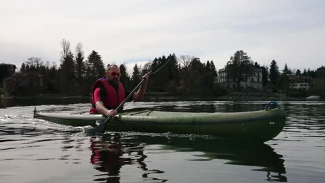 POV-Aufnahmen-Eines-Erwachsenen-Mannes-Mit-Gelber-Sonnenbrille-Und-Roter-Schwimmweste,-Der-Kajak-In-Einem-See-Rudert