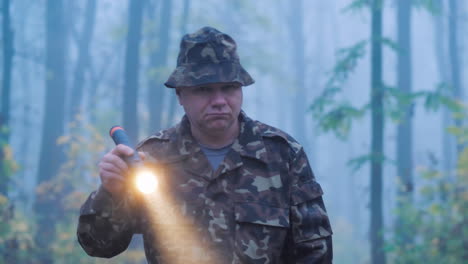 a man in camouflage is walking through the forest with a flashlight in his hand wet rainy weather in