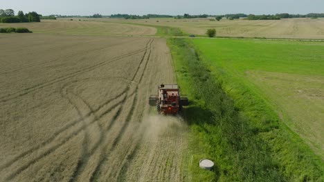 Aerial-establishing-view-of-combine-harvester-mowing-yellow-wheat,-dust-clouds-rise-behind-the-machine,-food-industry,-yellow-reap-grain-crops,-sunny-summer-day,-drone-shot-moving-forward,-tilt-down