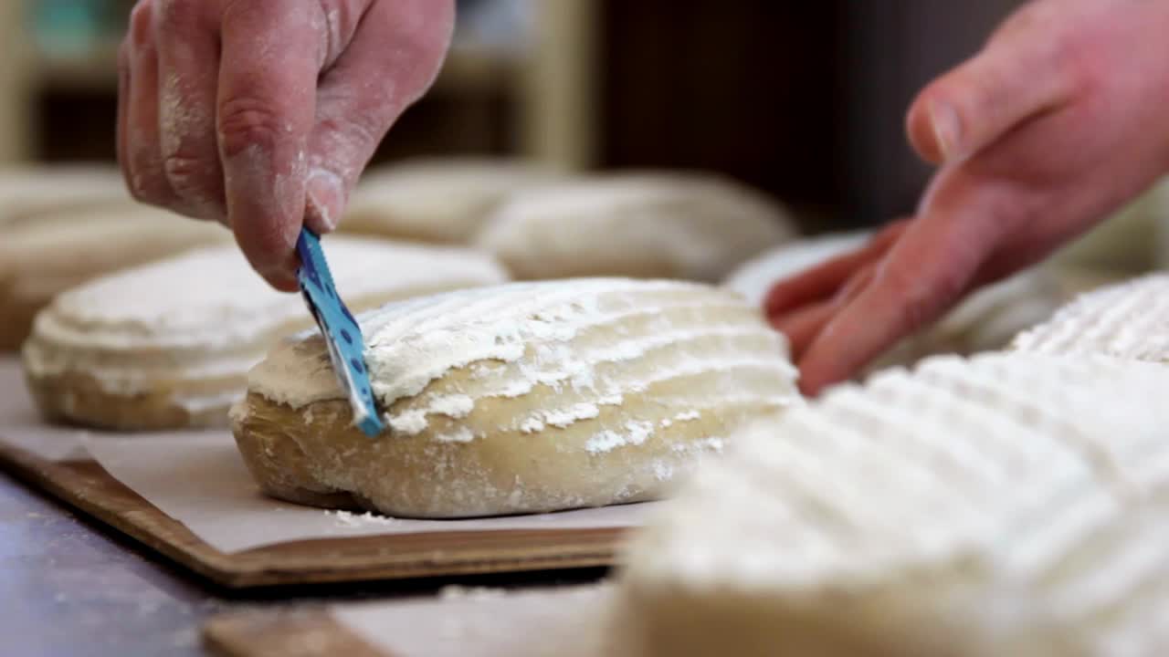 baker scoring proofed bread dough for the oven, close