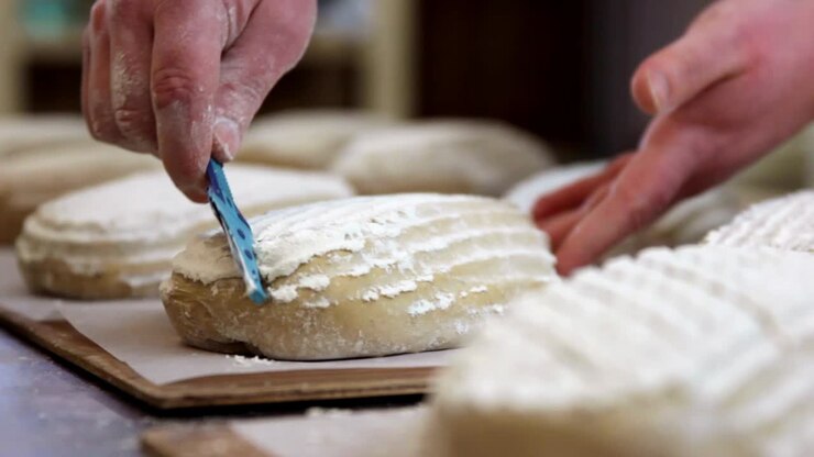 baker scoring proofed bread dough for the oven, close