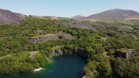 Vista-Aérea-De-La-Cantera-De-La-Mina-De-Pizarra-Dorothea-Ruinas-Del-Bosque-En-El-Valle-De-Snowdonia-Con-Un-Hermoso-Lago-Azul-Brillante