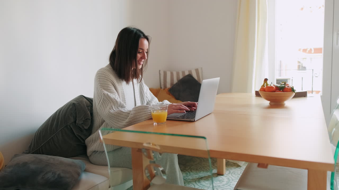 Giovane donna che lavora al laptop a casa con succo d'arancia