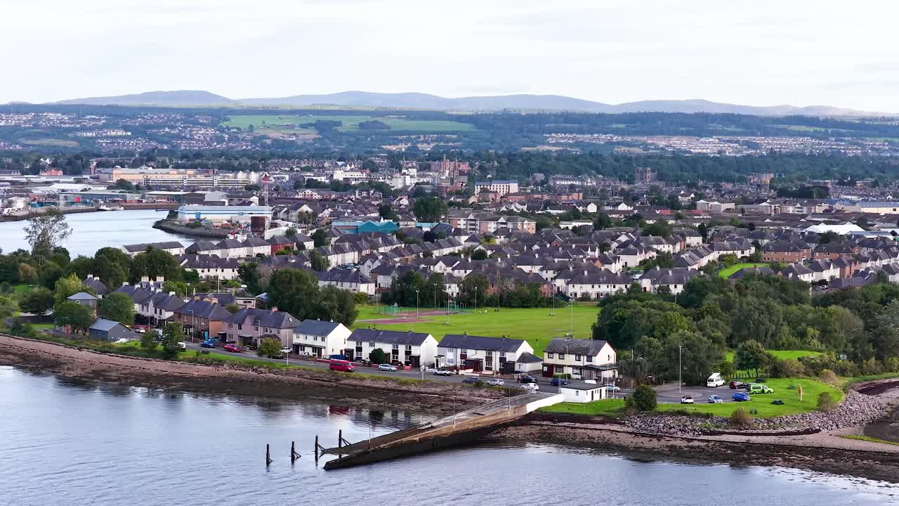 Drone camera pans over Dundee’s riverside houses, green spaces, and urban landscape in daylight