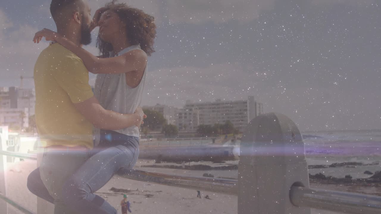 Pareja en una pose íntima, abrazándose y besándose junto a la barandilla de la playa para marketing de viajes, con un destello de lente.
