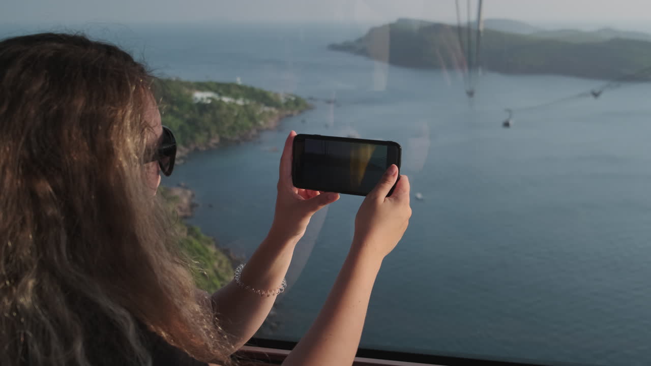 mujer tomando una foto desde un teleférico con vistas panorámicas al mar