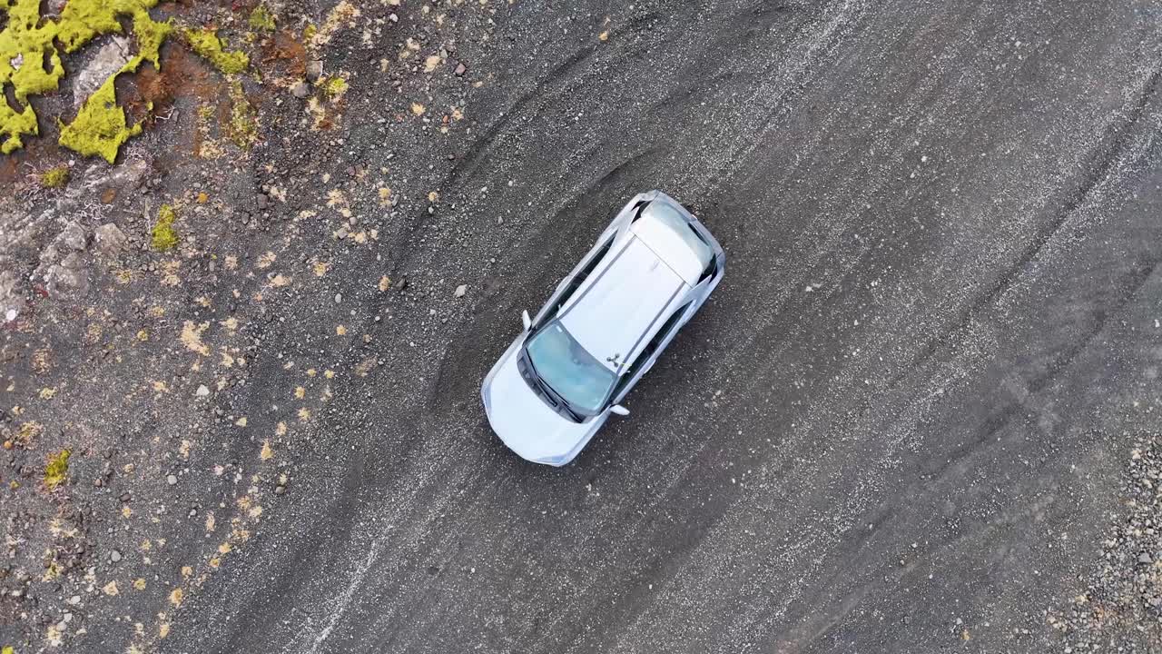 las imágenes aéreas capturan un coche blanco estacionado en un terreno desolado desde una perspectiva de avión no tripulado en espiral