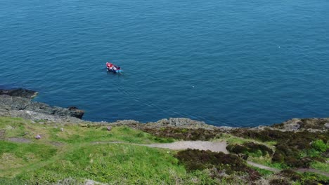 Small-fishing-boat-sailing-colourful-blue-ocean-water-view-from-Welsh-mountain-slope