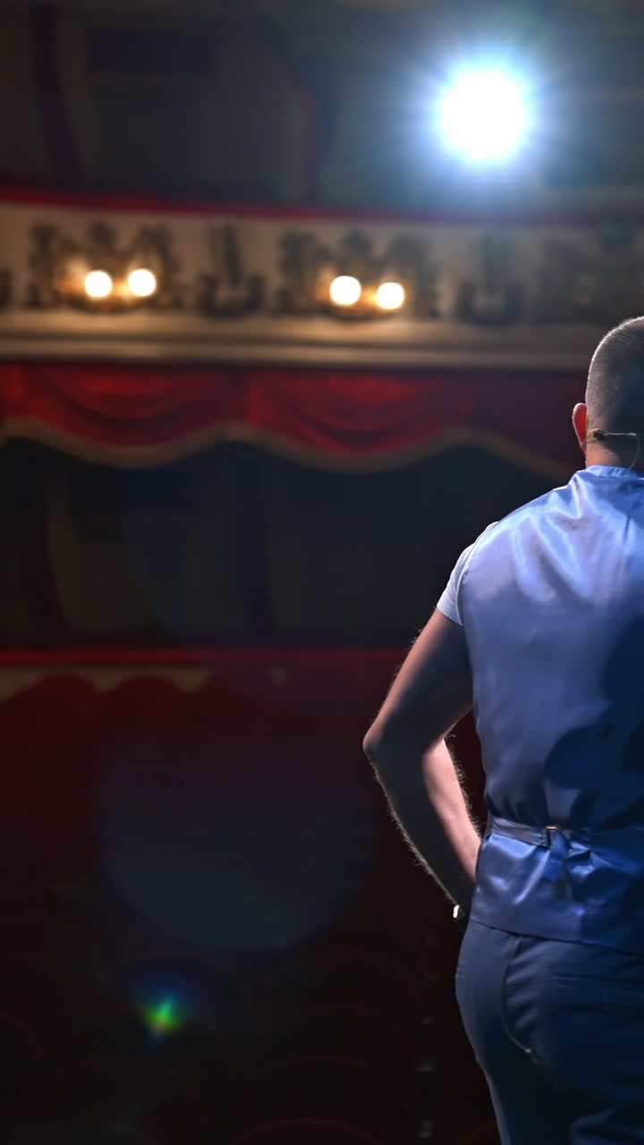 Actor rehearsing his role. Male speaker performing in front of empty auditorium in theater against bright spotlight. Back view. Vertical video