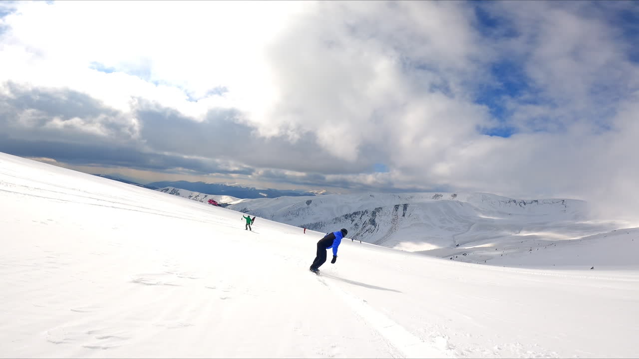 Following a sportsman snowboarding in the mountains. Stunning scenery under cloudy sky at backdrop.