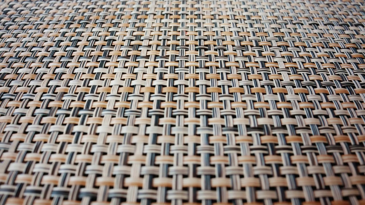 A detailed macro shot of a woven material reveals an intricate pattern of interlaced fibers in neutral tones