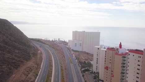 View-from-a-drone-flying-over-a-highway-with-a-mountain-on-the-left-side-and-the-hotel-zone-to-the-right-close-to-the-coast-showing-the-ocean-and-the-sky-in-the-background-in-Mexico