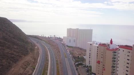 view from a drone flying over a highway with a mountain on the left side and the hotel zone to the right close to the coast showing the ocean and the sky in the background in mexico