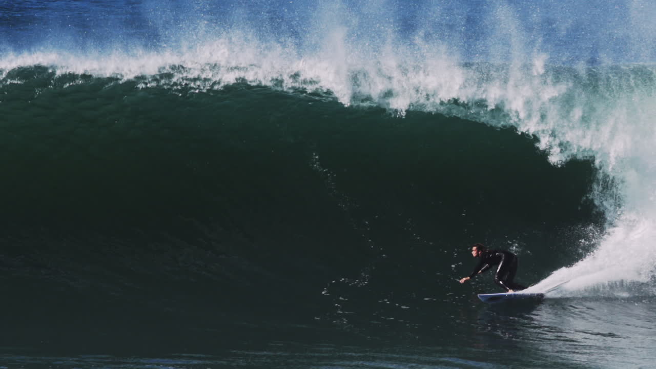 Backlit green wave barrels into darkness as surfer glides through foamy chute