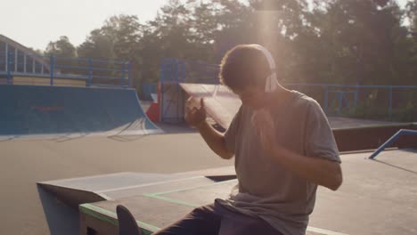 young man on skate park, sitting down and putting on some headphones