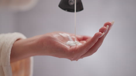 person pours liquid conditioner for hair into palm in shower. creamy hair conditioner drips onto female hand in spacious room with blurred background