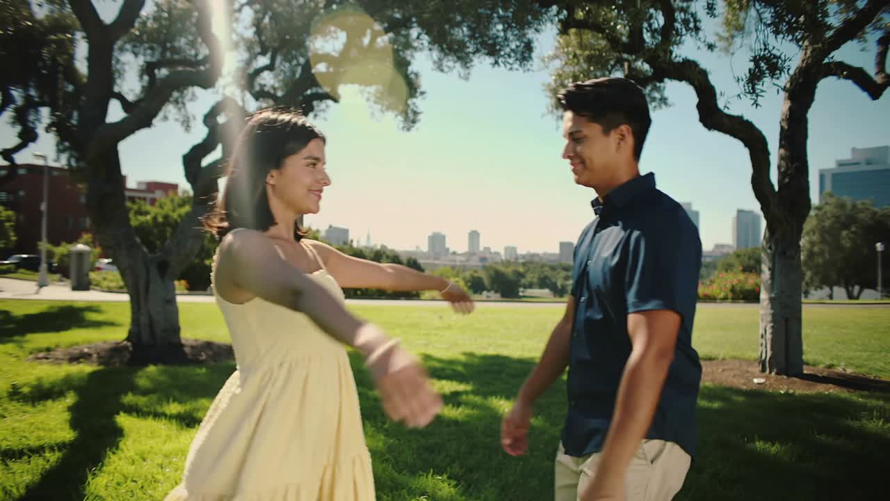Spotting woman in yellow dress, man in navy polo embracing in sunny park, reuniting near skyline