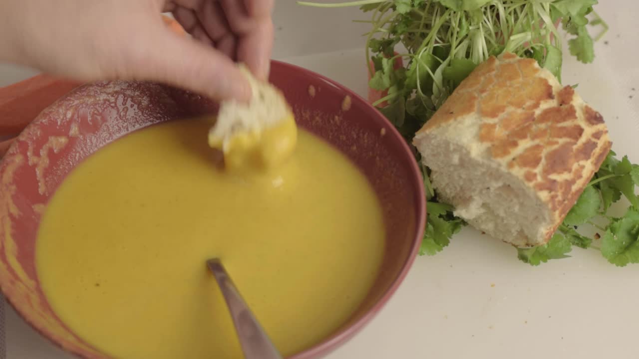 Hand dipping bread into fresh carrot and coriander soup