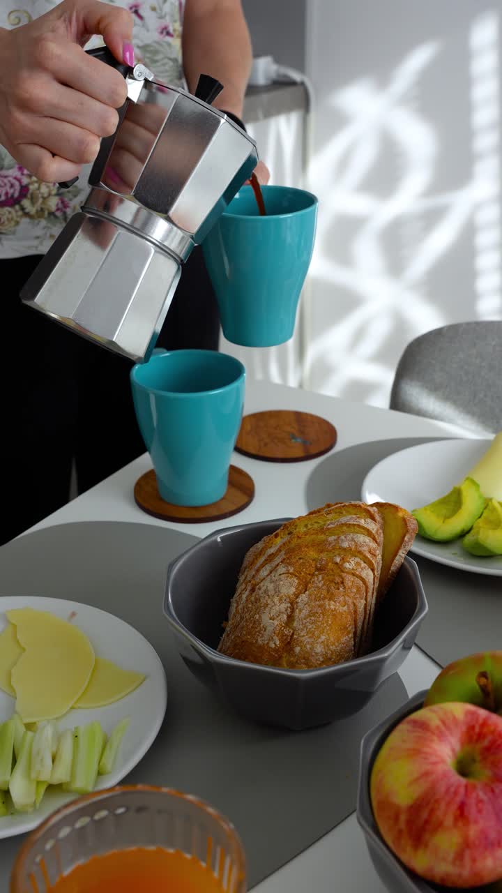 Coffee poured from moka pot in blue mugs near breakfast food on table, vertical
