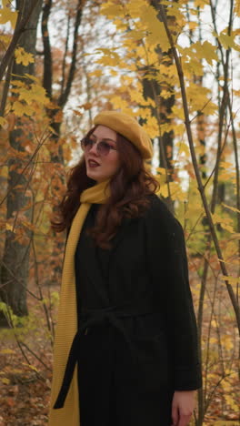 dama elegante en boina amarilla y silenciador camina a través de un camino del bosque, mirando a su alrededor como las hojas de otoño se balancean suavemente con el viento, inmersos en la belleza tranquila de la temporada