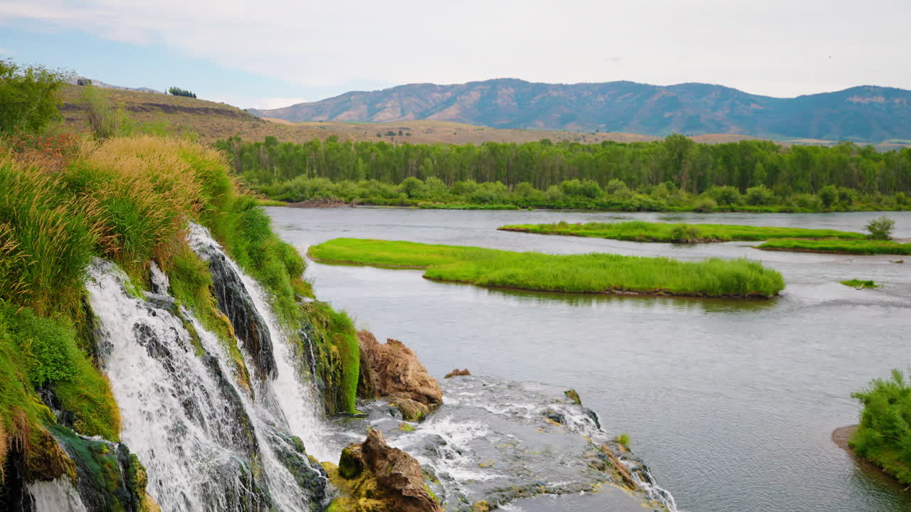 Scenic Waterfall Cascading into a Lush River Landscape with Distant Mountains