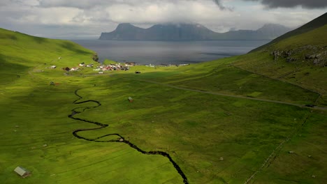 river meandering down mountainside to gjógv coastline in faroe islands, aerial view