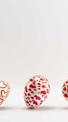rolling heart-patterned eggs on white background. vertical looped animation