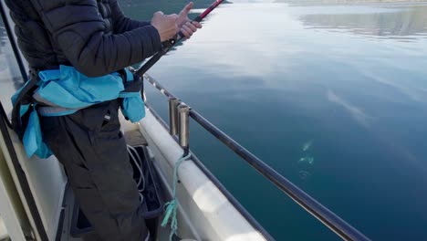 man on boat reeling fishing rod and catching two fish from a lake in norway